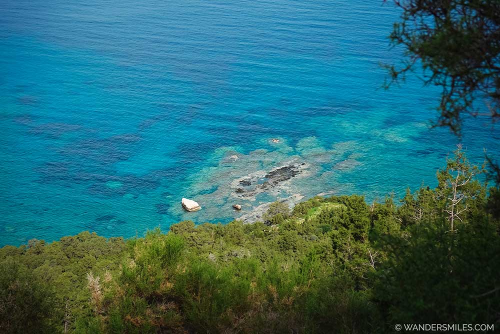 Hiking Akamas Peninsula in February. Coastal views show vibrant blue turquoise waters contrasting with the lush green edge.