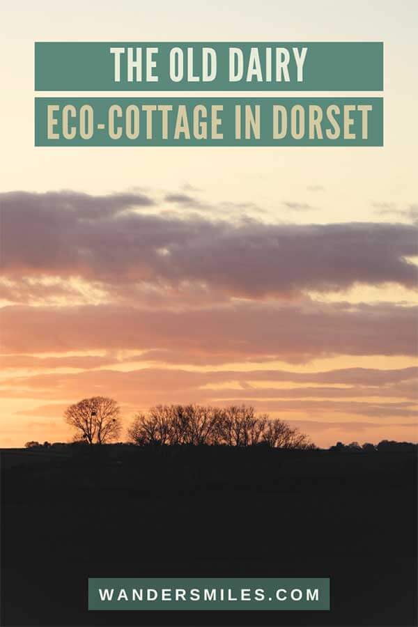 Image of peachy-purple sunset with black tree silhouettes. Text overlaid text “The Old Dairy Eco Holiday Cottage in Dorset”