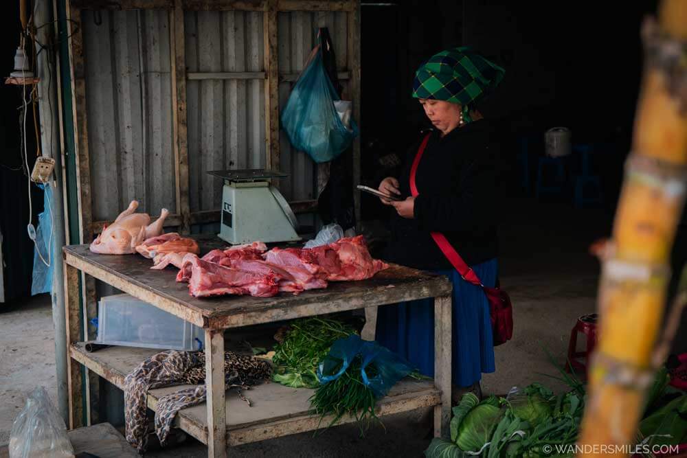 H'Mong butcher in a rural village near Sapa with meat on the table. She wears a bright woven scarf and it on her mobile phone