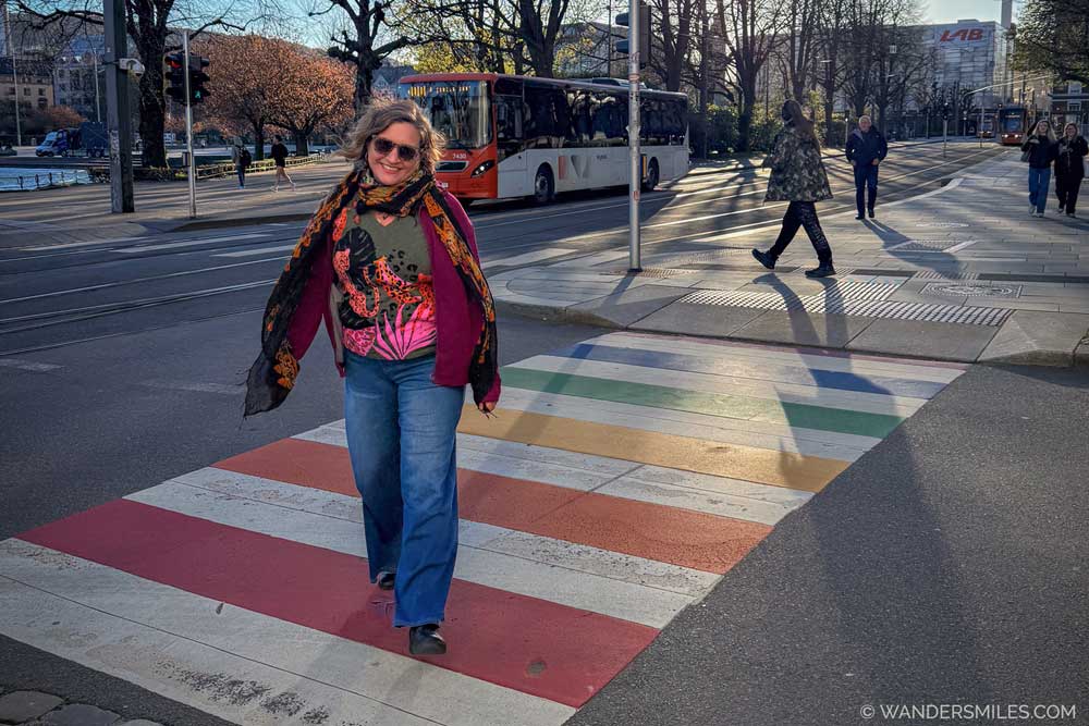 A woman walking on a rainbow-coloured pedestrian crossing in Bergen, wearing bright clothing and jeans