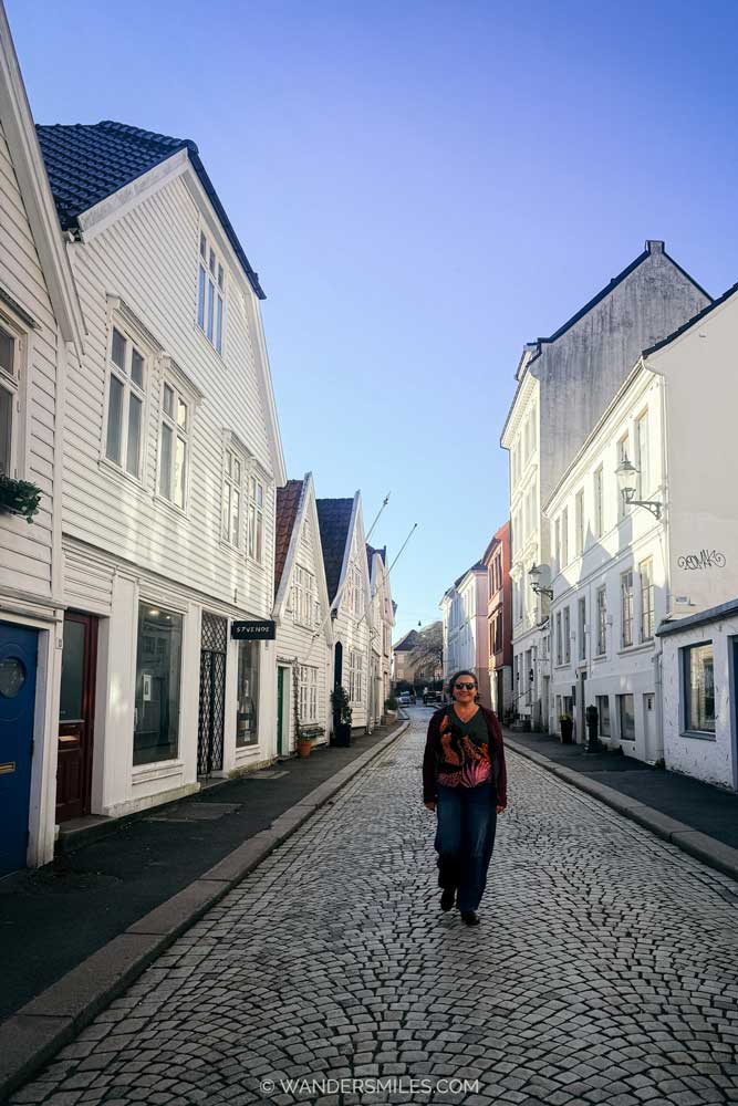 Woman walking down Lille Øvregaten, a street with white painted wooden houses in Bergen, Norway