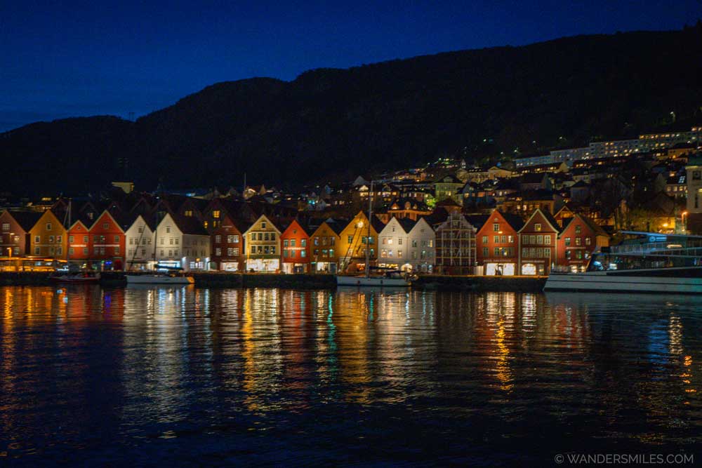Bryggen Wharf at night with the coloured houses reflecting in the water, dark ble sky and silhouette of a mountain