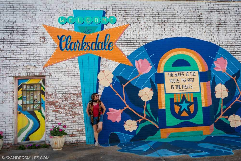 A woman in shorts leaning against a mural with "Welcome To Clarksdale". Feature photo for the blog "Cool things to do in Clarksdale"