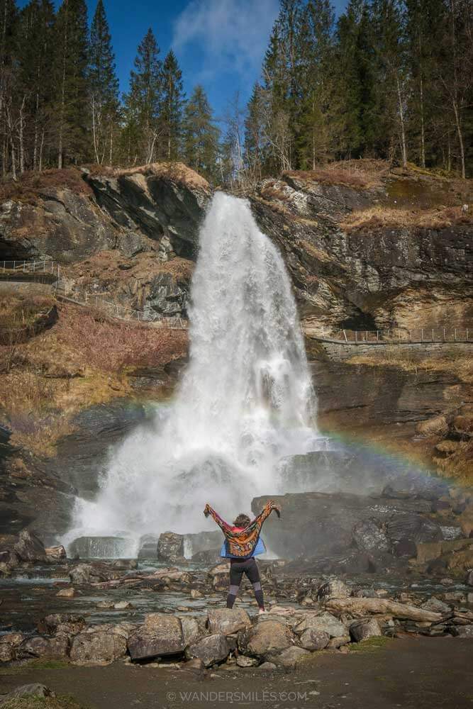 Woman at the bottom of Steinsdalsfossen waterfall in Hardanger with a rainbow at the bottom of the flowing water