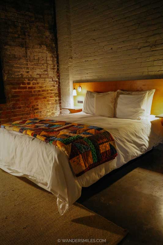 Dark bedroom in Travellers Hotel, Clarksdale, with a thrown on the bed and exposed brick walls