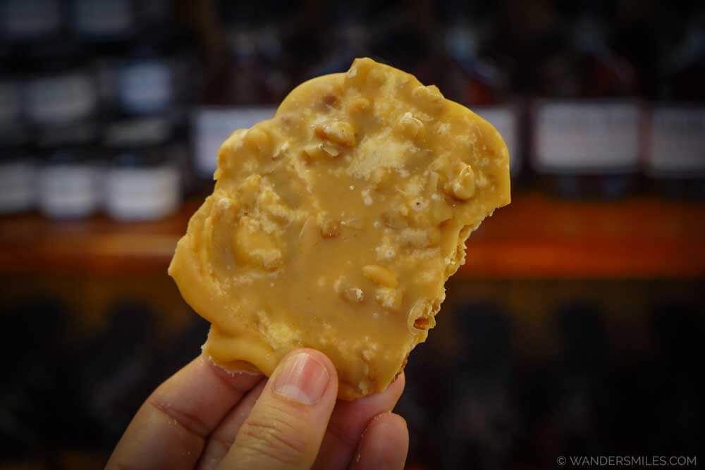 Fingers holding Praline Brittle: A sugary, creamy Southern confection made with pecans, sugar, butter, and cream