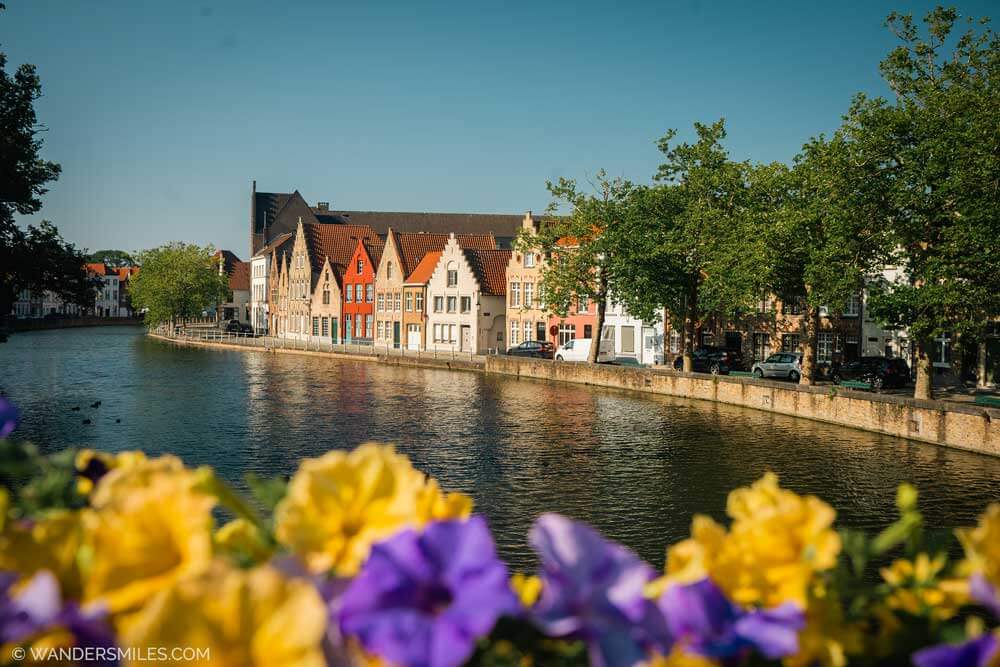 Gabled houses along Potterierei canal in Bruges with flowers in the forefront in planters on the bridge.