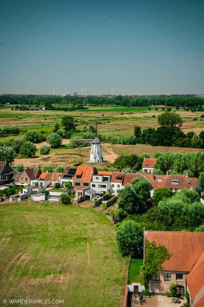Countryside views from the top of the tower of Church of Our Lady in Damme, with houses, a windmill and green pastures. A must-do on a day trip to Damme.