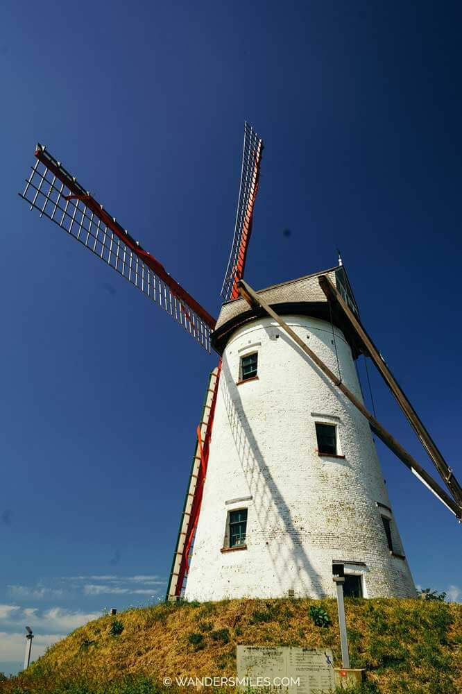 Exterior of the white Hoeke Windmill in Damme on a mound with blue skies