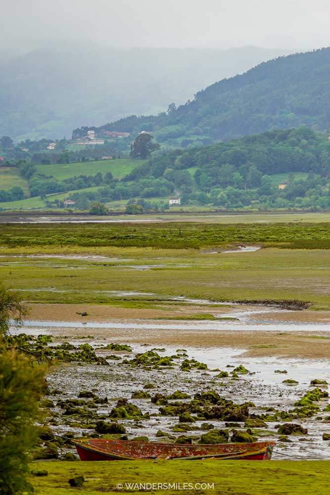 La Isla del Bornizal in the Ría de Villaviciosa Natural Reserve, Asturias. Photo shows the estuary with mountains on the other side and a small boat in the front.