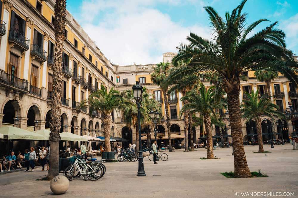 Plaça Reial is a famous 19th-century neoclassical square in Barcelona's Gothic Quarter, just off La Rambla, with palm trees.