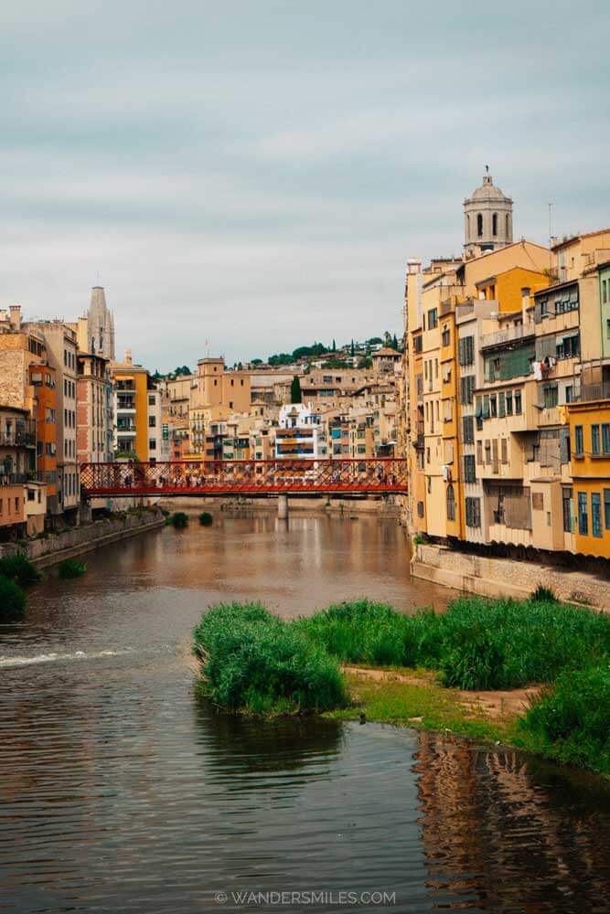 View down Onyar River, Girona. Shows the Pont de les Peixateries Velles (red bridge) and stone coloured buildings