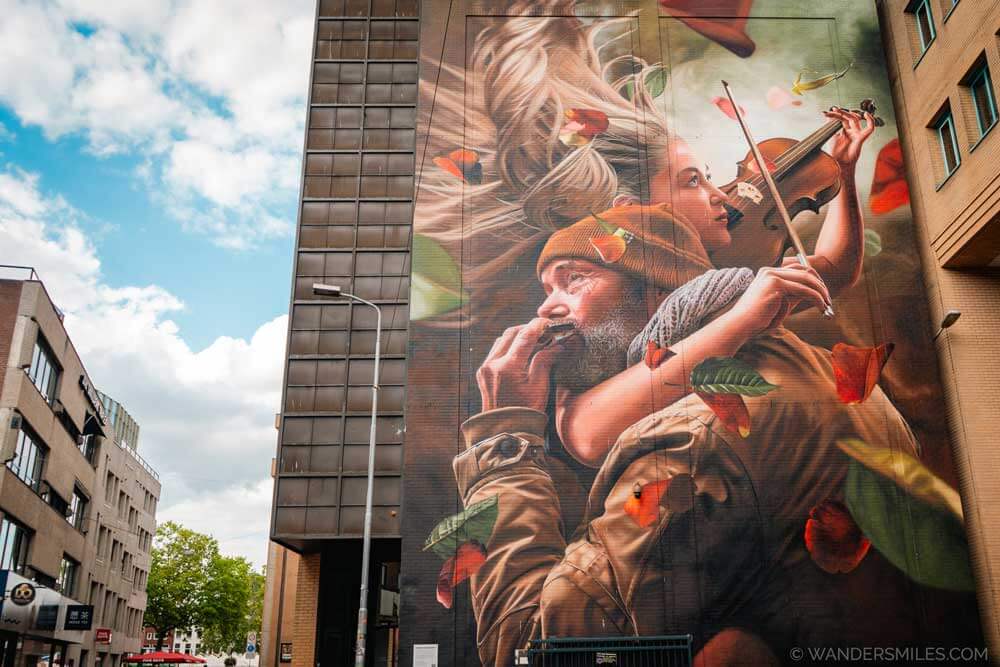 Mural: Echoes of Harmony by Studio Giftig. Shows a street musician and a concert violinist in red shades.
