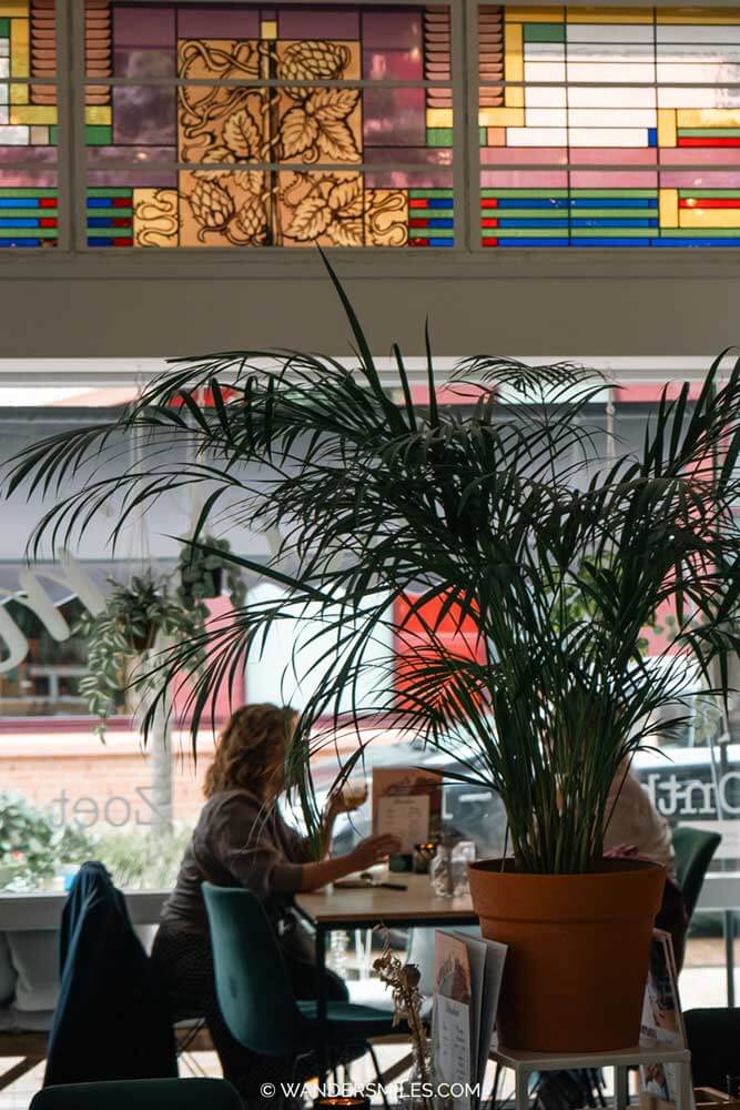 Two women having lunch in Smeer'M cafe in Tilburg with large plants and stained glass windows